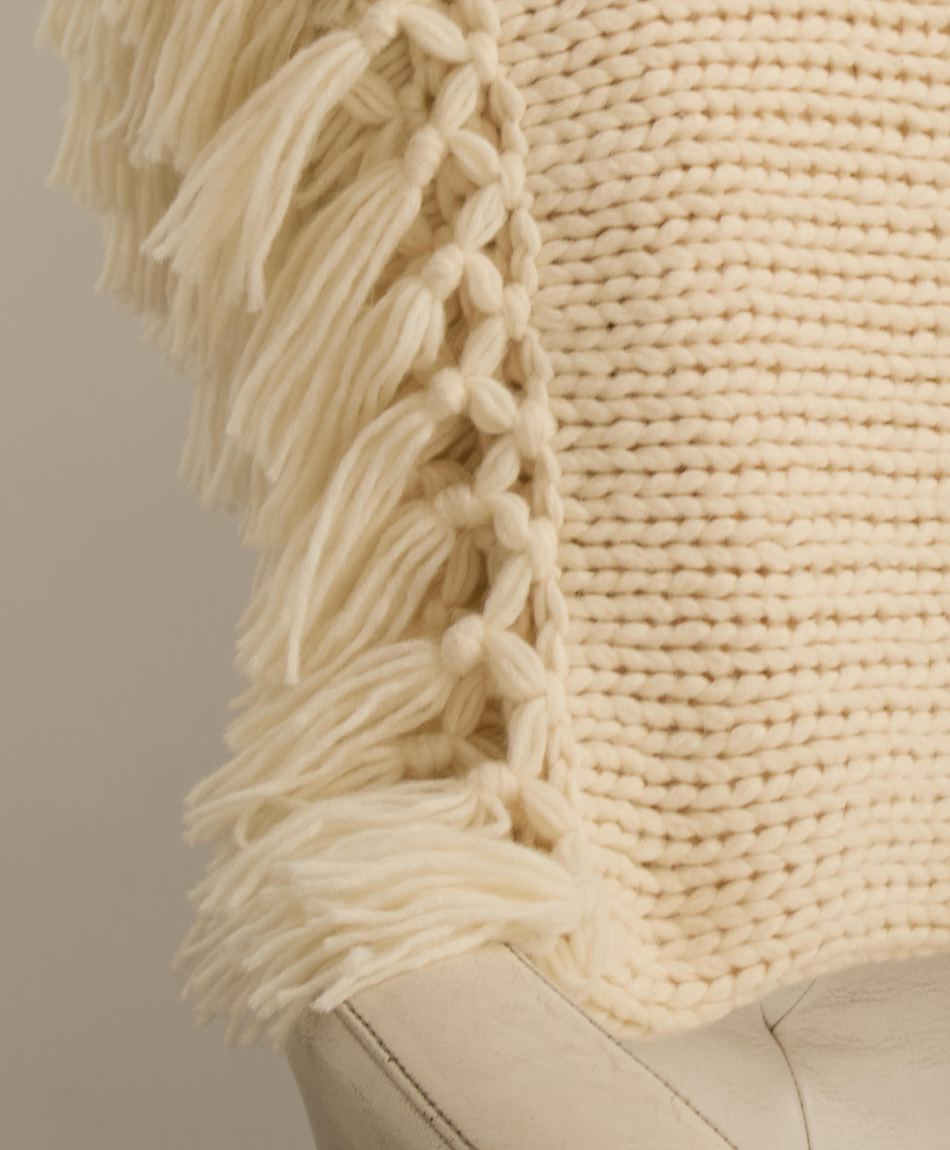 Close-up of an ivory chunky-knit throw, with knotted tassels along its edge